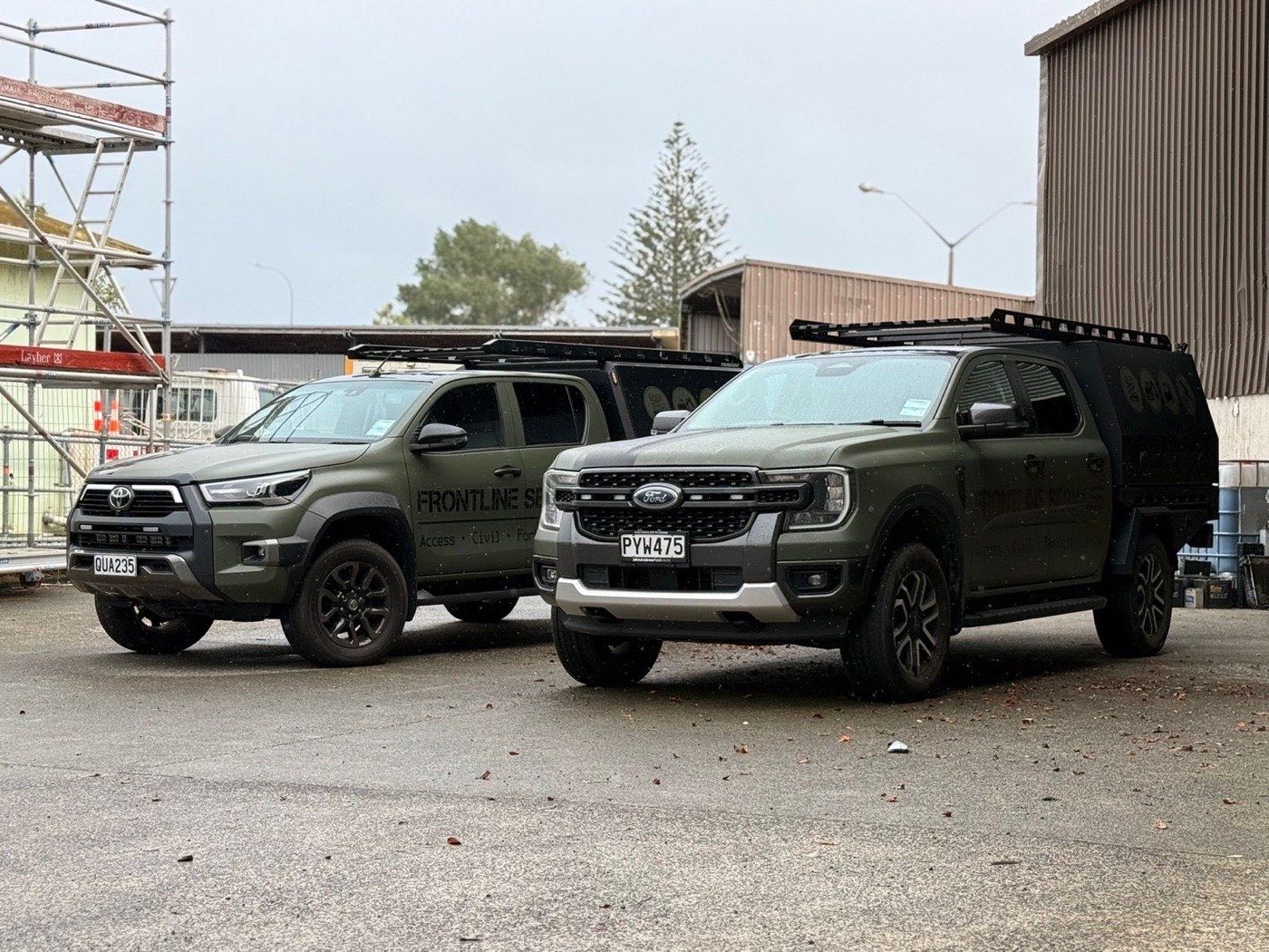 Two Frontline Services utes in the field-green livery, loaded with racks and service canopies